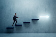 © Who is Danny - Side view of young business man climbing illuminated arrow stairs to success on concrete wall background in interior. Financial growth, career development and forward concept.