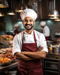 Happy male Indian chef with crossed arms wearing white dress and maroon apron on kitchen background