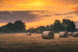 Fototapeta Miasto - Pomarańczowy letni wschód słońca nad polem, na którym leżą bale słomy
