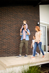 Wall Mural - Family with a mother, father, son and daughter walking by the wall of brick house