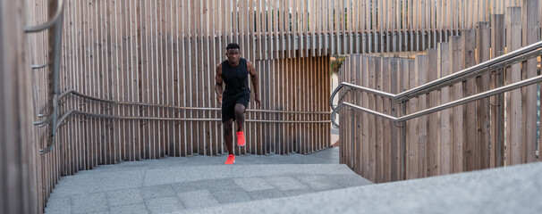 Canvas Print - Confident African man in sportswear looking concentrated while running up by stairway outdoors