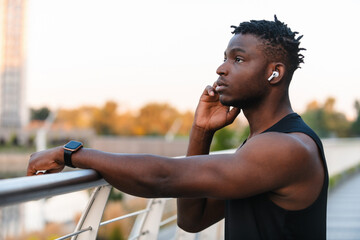 Canvas Print - Handsome African man in sportswear adjusting his headphones while resting after training outdoors