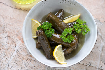 Wall Mural - Greek dolmades served with fresh parsley and lemon wedges in a grey bowl, horizontal shot on a pinkish granite background, elevated view