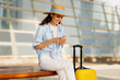 © Prostock-studio - Smiling young european woman in hat with suitcase, typing on smartphone, enjoy trip at station