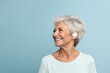 Happy 60 year-old woman with hearing problems with a new hearing aid looks to the side on a blue background. Grandma is glad that the clarity of the sound has improved and now she hears well