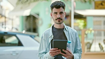 Poster - Young hispanic man smiling confident using touchpad holding bottle of water at street