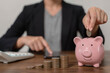 The thrifty businessman puts coins in a pink pig shaped savings box. The idea of saving money is to invest in the future. Year-end tax and life insurance savings