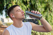 Young Caucasian sportsman drinks from his water bottle while listening to music with earphones.