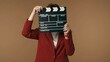 © kinomaster - Medium isolated shot satisfied, happy and relaxed young woman holding a closed movie clicker, slate, clapperboard in front of her face.
