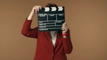 Medium isolated shot satisfied, happy and relaxed young woman holding a closed movie clicker, slate, clapperboard in front of her face.