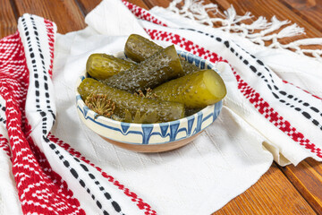 Wall Mural - Cucumbers pickled in Romanian traditional clay bowl and traditional towel on wooden table