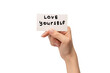 Love yourself text on a card in a woman hand isolated.