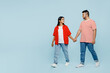 Full body side view young couple two friends family Indian man woman wear red casual clothes t-shirts together hold hands walk go strolling isolated on pastel plain light blue cyan color background.