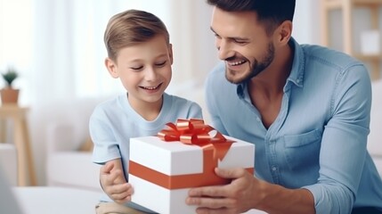 Cute son is giving a gift box decorated with ribbon to the happy father on blurred home background, concept of happy fathers day, with copy space.