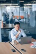 © Yaroslav Astakhov - asian businessman working on laptop in office with colleagues in the background. Business concept