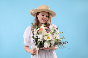 Canvas Print - Beautiful woman in straw hat with bouquet of flowers on light blue background