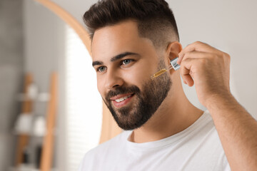 Poster - Handsome man applying cosmetic serum onto his face in bathroom