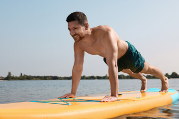 Wall Mural - Man practicing yoga on SUP board on river