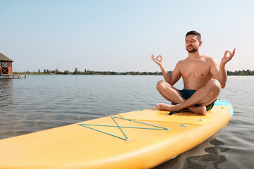 Wall Mural - Man practicing yoga on SUP board on river