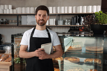 Wall Mural - Happy seller with notebook and pen near showcase in bakery shop