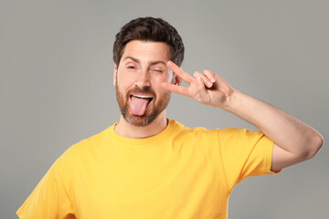 Canvas Print - Man showing his tongue and V-sign on gray background