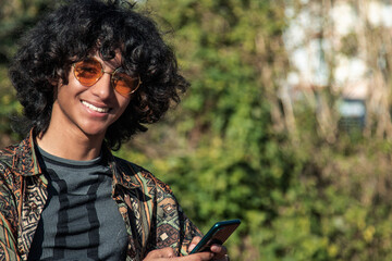 Wall Mural - young man smiling with mobile phone outside