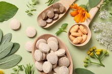 Different pills, herbs and flowers on light green background, flat lay. Dietary supplements