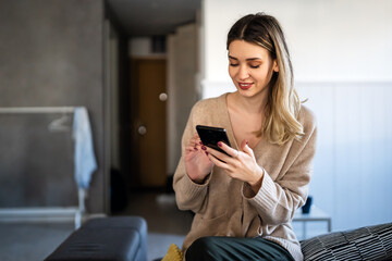 Wall Mural - Smiling young woman chatting in social networks, working, using mobile applications at home.