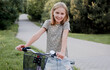 © tan4ikk - Cute preteen girl with bycicle outdoors looking at camera and smiling. Pretty child with bike at city street at summer park