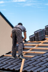 Wall Mural - construction worker installs a fired ceramic tile on the roof of family house