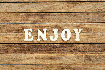 The word Enjoy composed of wooden letters on a wooden background.
