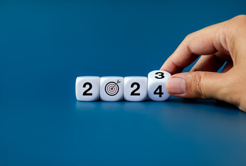 Wall Mural - 2024 New year business goal and trend concepts. End of 2023 to begin 2024 year numbers calendar with target dart icon on white cube blocks flipping by human hand isolated on blue banner background.