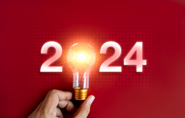 Shining 2024 calendar year numbers, neon style with creative trend light bulb holding by businessman's hand on digital network and red background. Happy 2024 New Year greeting card with light bulb.