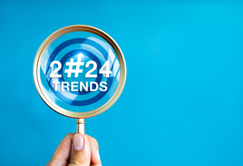 Wall Mural - 2024 Trend concept. 2024 year number with hashtag symbol in magnifying glass lens, holding by hand, on blue background with copy space. Focusing on the year 2024 for online digital trends update.