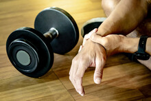 Male Athlete Massaging His Wrist And Hand Suffering From Wrist Pain Caused By Sprain Or Joint Fracture From Overweight Dumbbell Lifting In Fitness Gym. Sport Injury Concept