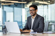 © Liubomir - Young successful Arab businessman in business clothes works inside the office with a laptop, satisfied with the results, the boss in glasses types on the computer keyboard