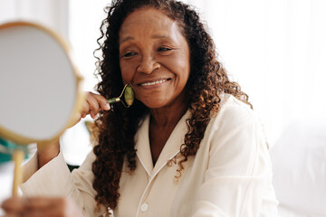 Wall Mural - Anti-aging skincare routine: Mature woman using a jade roller on her face