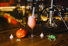 Halloween Holiday Accessories In A Restaurant At A Party: Pumpkin Lantern, Candles, Spider, Cocktail, Hookah On A Wooden Table. Photography, Tradition.