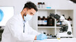 © Siphosethu/peopleimages.com - Scientist and research or medical engineer doing experiments to create a cure in a lab while wearing a mask. Healthcare professional working with science equipment and writing notes in a laboratory