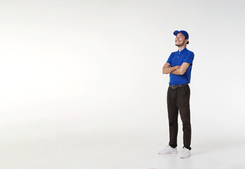 Wall Mural - Smiling asian delivery man in blue uniform standing with arms crossed isolated on white background. looking up copy space. Full length portrait.