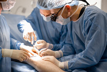 Three Confident Surgeons Performing Surgical Operation On A Patient's Knee In Operating Room. Concept Of Real Surgery And Invasive Treatments