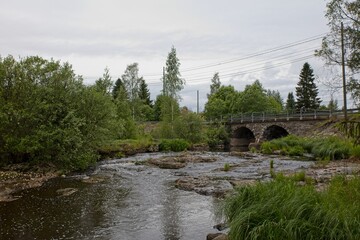 Two arch old stone bridge over Hirvihaaranjoki river in cloudy weather in summer, Hirvihaara, Finland.