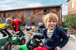 Cute adorable blond shaggy happy kid boy enjoy having fun riding toy tractor playing countryside farm house yard with friends. Childhood happiness country playground. Funny person emotions expression