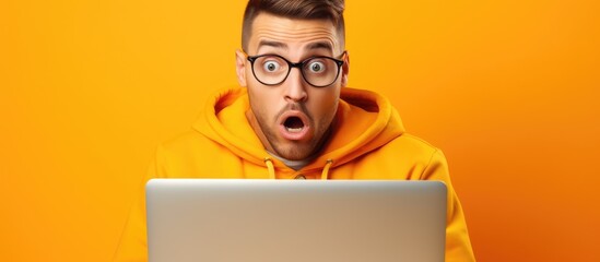 Surprised young freelancer in 20s wearing an orange vest and glasses using a blank laptop in a yellow studio