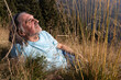 © Guzel - Adult gray-haired man with long hair resting on a field with tall grass in the evening sunlight
