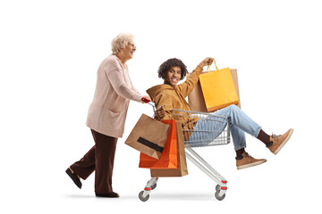 Poster - Grandmother pushing a young african american man with shopping bags inside a shopping cart