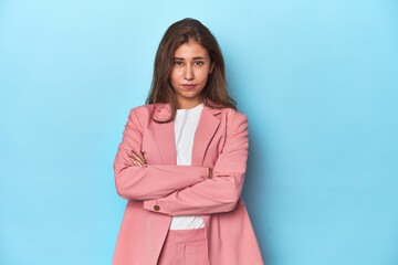 Wall Mural - Teen girl in chic pink suit on a blue background unhappy looking in camera with sarcastic expression.