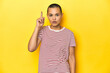 © Asier - Shaved head woman in red striped tee, yellow backdrop having an idea, inspiration concept.