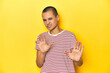 © Asier - Shaved head woman in red striped tee, yellow backdrop rejecting someone showing a gesture of disgust.