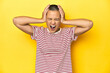 © Asier - Shaved head woman in red striped tee, yellow backdrop covering ears with hands trying not to hear too loud sound.